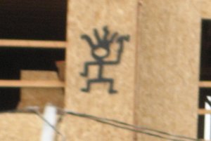 Embellished stick figure, spray-painted on plywood on a partially-constructed building.