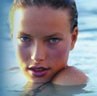 Blonde woman lifting her head out of a swimming pool, giving a "come hither" look.