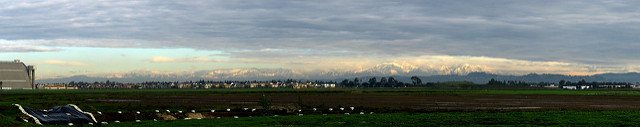 Wider view of the same snow covered mountains lit up by the sun, with clouds above them. 