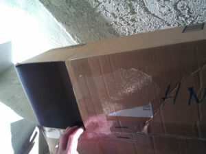 A cardboard box with a hole in the side. The inside back of the box is in shadow, but a small circle of light is visible on it.
