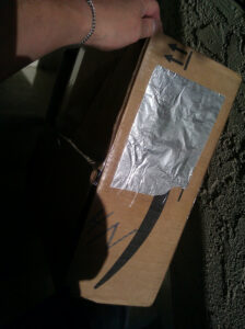 A cardboard box with a piece of foil taped over it.