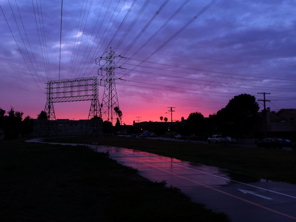 Bluish clouds, a magenta horizon, and silhouettes of electrical towers and lines, all reflected in a path.