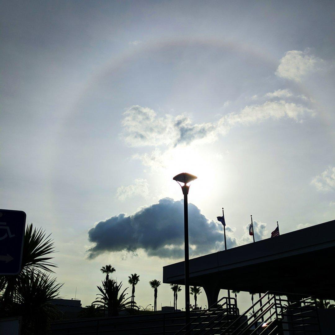 A bright circle around the sun, centered on the silhouette of a lamp post. An open roof is silhouetted in the foreground, and a dark cloud in the background below the sun.