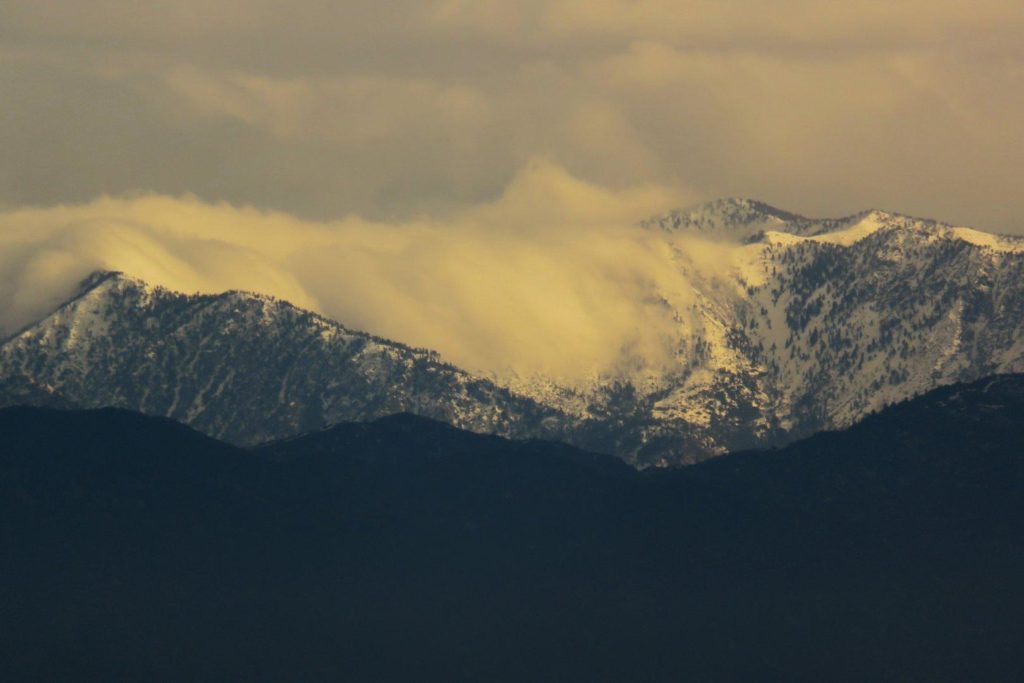 Snowy mountains in the distance with clouds flowing over the ridge.