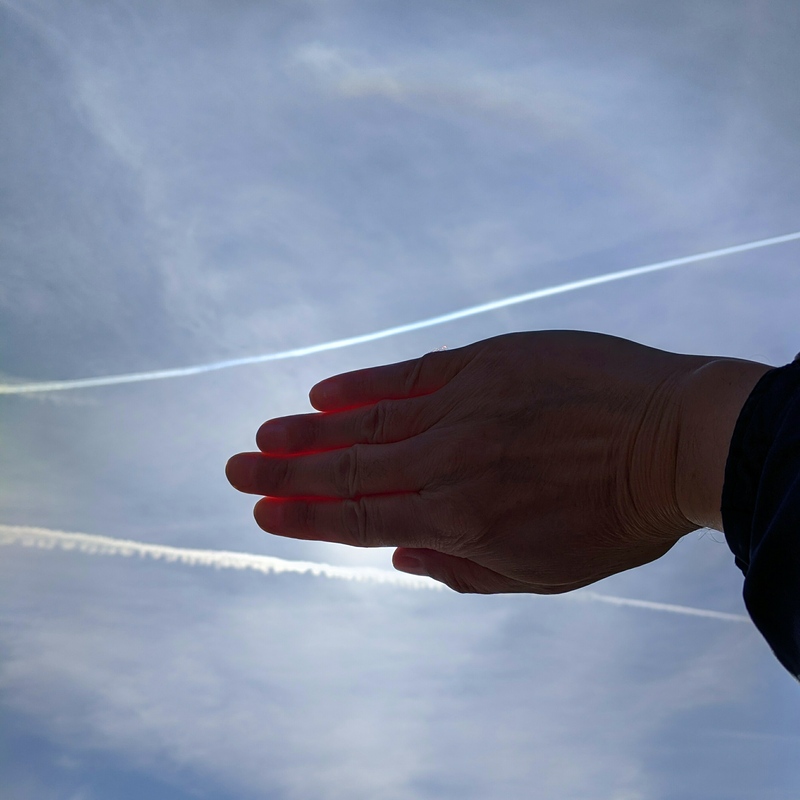 Slightly brighter arcs around the sun, and a couple of sharp contrails crossing the middle, with a hand blocking the sun.