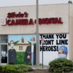 Camera shop with windows painted with American Gothic with six feet of social distancing and face masks, and a thank you message to front line heroes in scrubs.