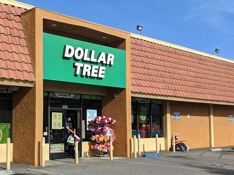 Someone sitting outside of a store with a guitar and a face mask.