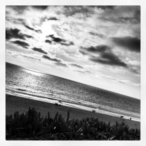 Black and white image of the ocean and clouds tilted so that a foreground hill is horizontal.