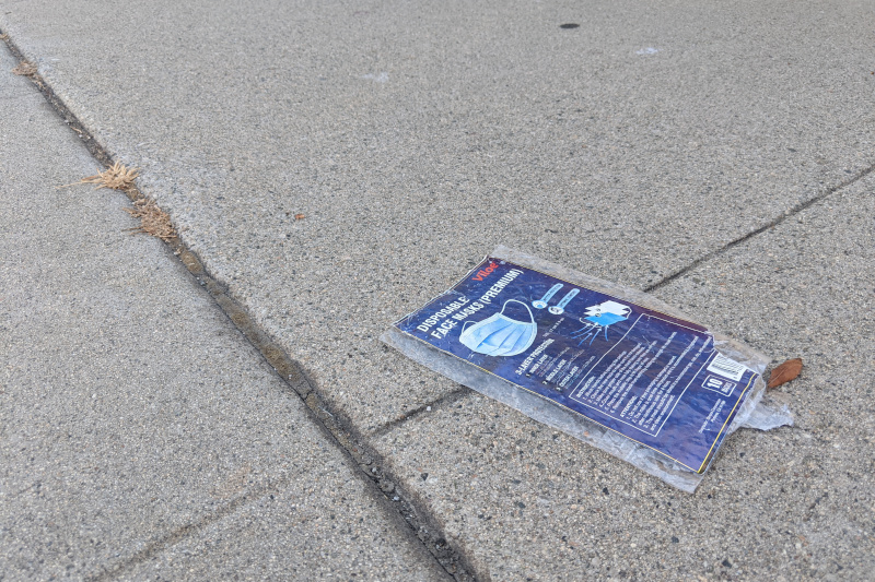 A bag of disposable face masks, discarded on the sidewalk.