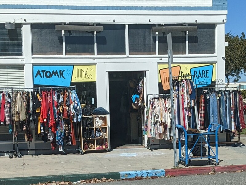 Thrift store with "Atomic Junk" and "Rare Funky Finds" painted on its windows and racks of clothes out on the sidewalk.