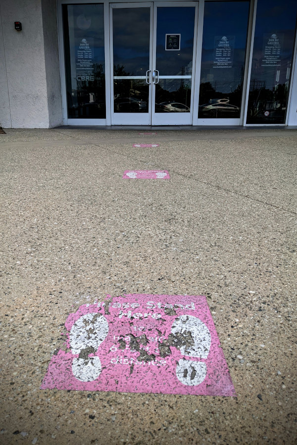 Faded and broken Stand-6-Feet-Apart labels on a sidewalk, leading to a doorway.
