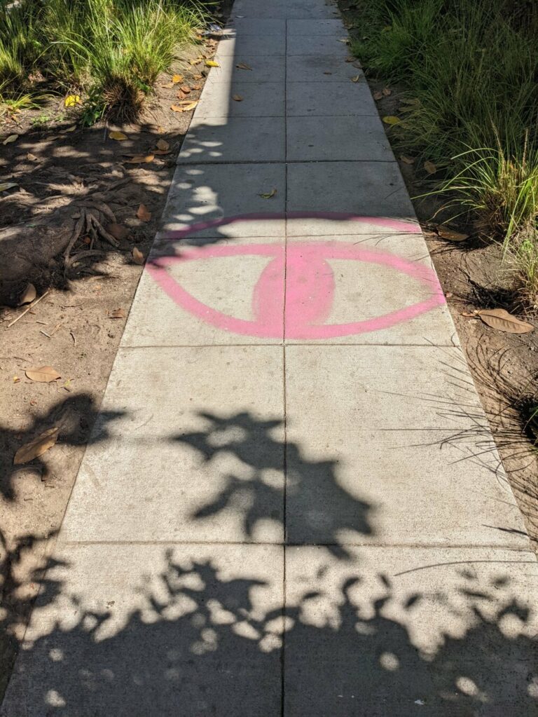 Concrete sidewalk stretching away from the camera, a stylized eye painted across it in red.