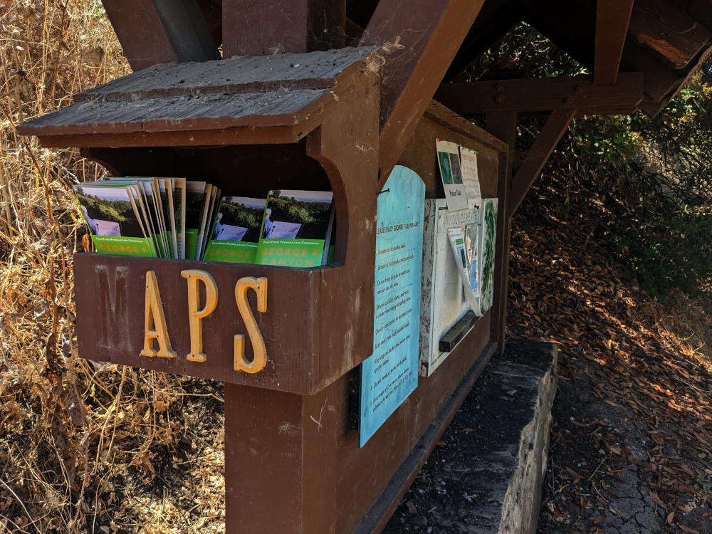 Information board with a small box of folded paper maps labeled MAPS, except the M has fallen off.