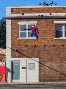 The same wall again. It's another sunny day, and a narrow shadow streaks diagonally across the bricks. This time, the Spider-Man climbing out of the upper-level window is bright blue and red, no signs of scratches, but the Superman silhouette at ground level is gone, replaced with a featureless white door-sized rectangle and a rather verbose sign that boils down to No Trespassing.