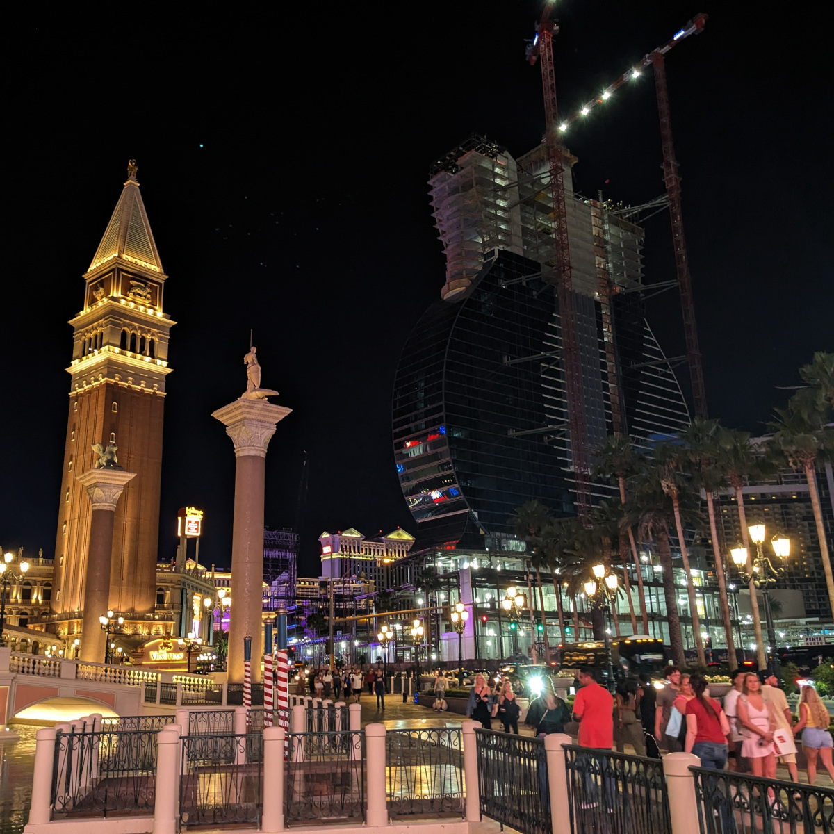 Night scene in Las Vegas. At the left, replicas of all the major landmarks of Venice are crammed into a small area. Off to the right, a tower is under construction in the shape of an upright guitar.