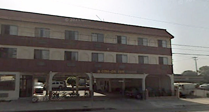 Backlit view of a three-level hotel building with a pass-through driveway. Above the driveway you can barely see a circle and the letters "COM-ON INN" in roughly the same style as the old Comfort Inn logo.