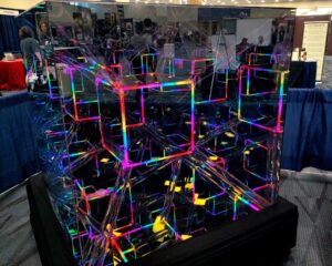 A sculpture of mirrors and LED strip lights, in the form of a hypercube tesseract, reflecting itself on and on forever.